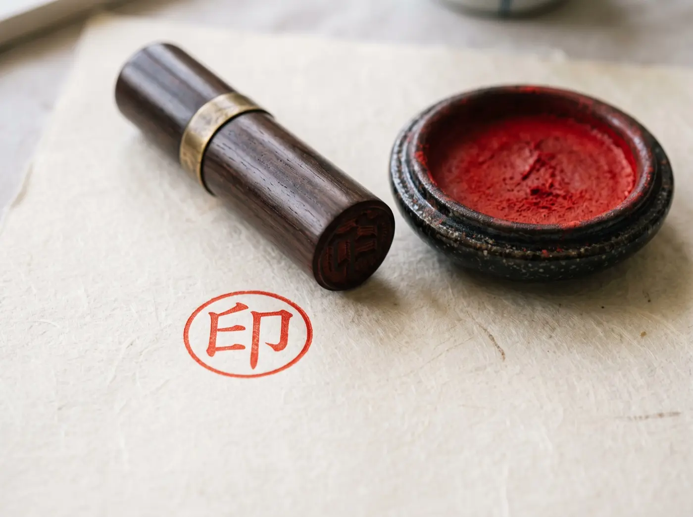 A hanko seal and its red ink pad on washi paper, beside the seal's fresh impression.